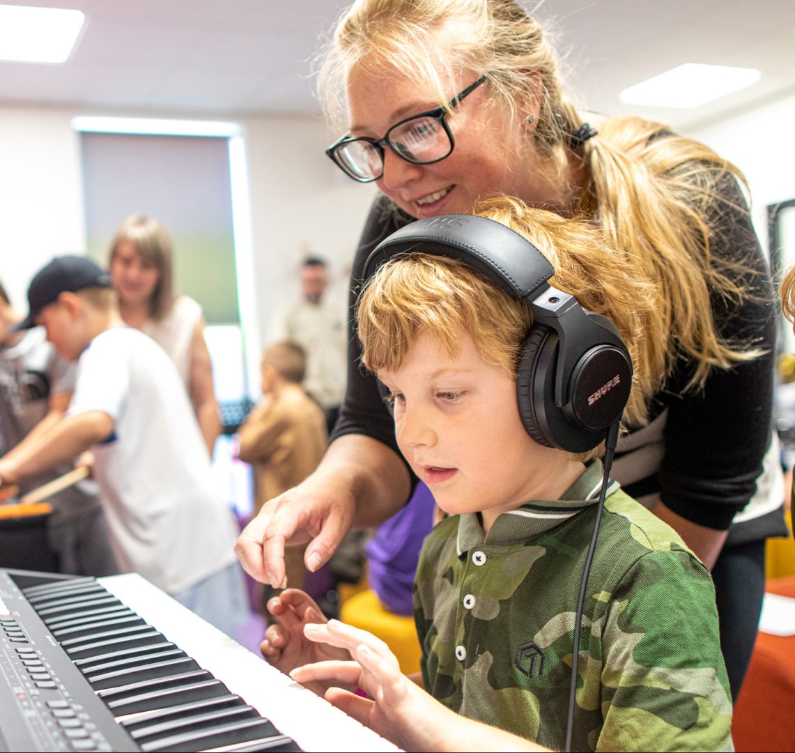 Photo of a young person playing the keyboard with an adult helping them